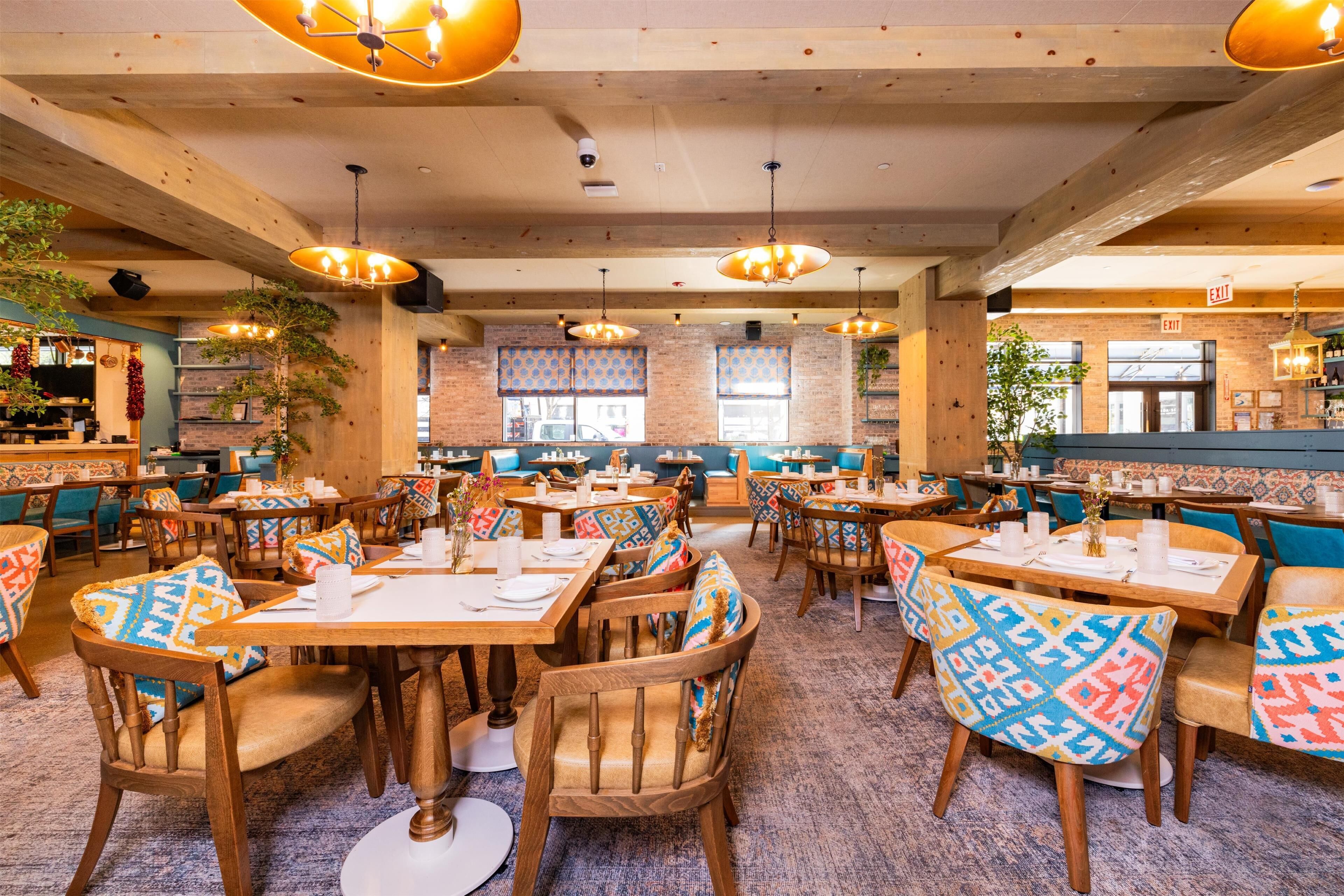 A restaurant with wooden tables and chairs, multiple hanging lights, and a brick wall.