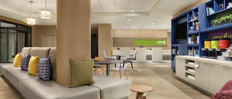 A modern hotel lobby with a seating area, a reception desk, and a coffee station.