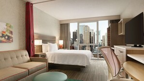 Ein Hotelzimmer mit Bett, Schreibtisch, Sessel, einer Couch und Blick auf die Stadt.