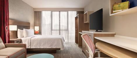 Una habitación de hotel con cama, escritorio, televisor, silla y sofá.