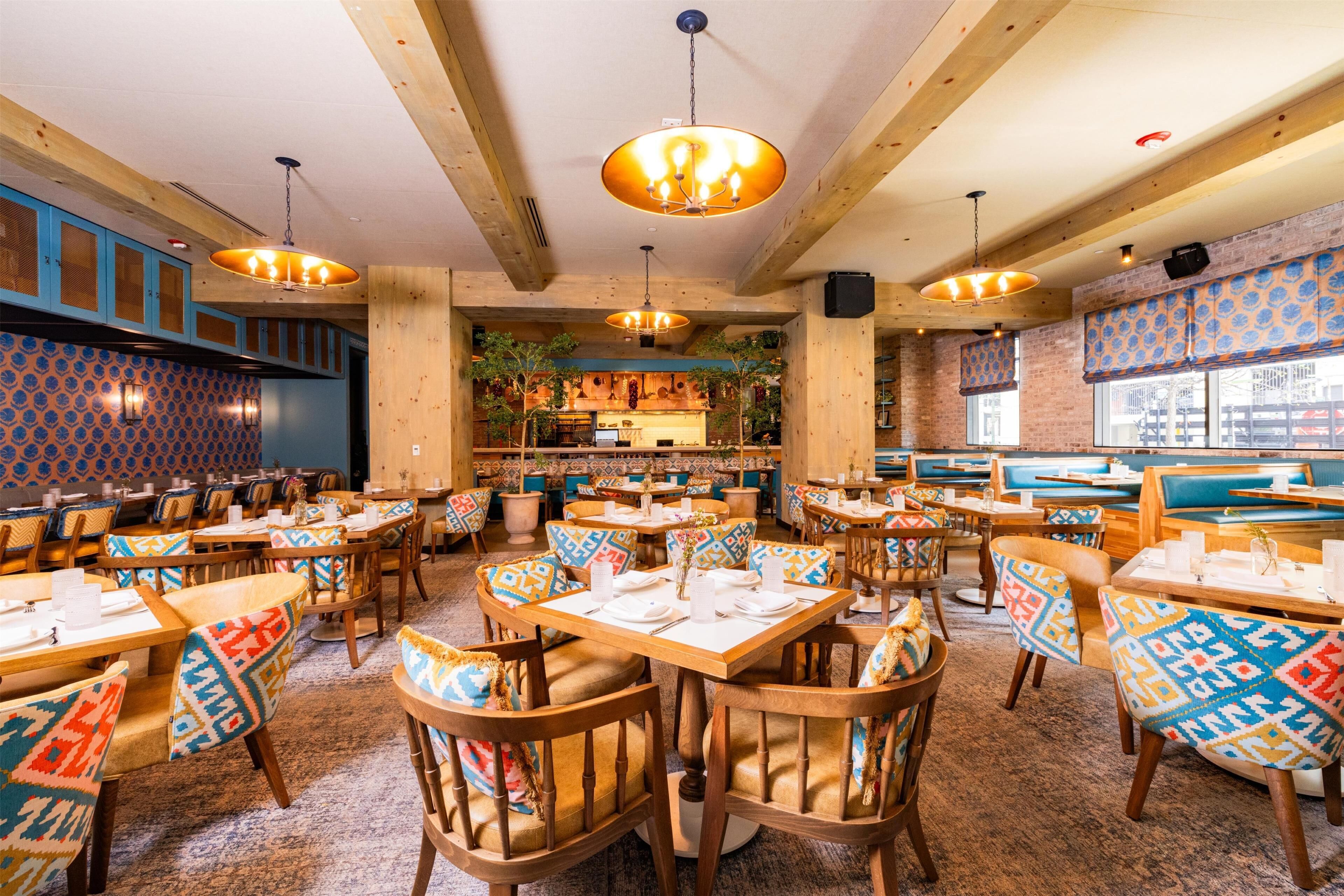 Un restaurante con mesas y sillas de madera, cojines estampados y lámparas colgantes.