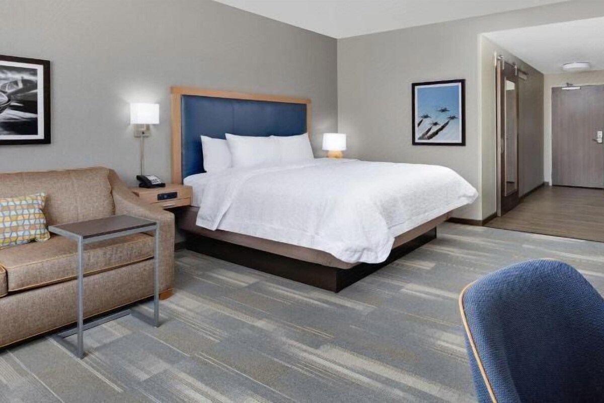 A hotel room with a bed, a desk, a chair, a sofa, and a television.