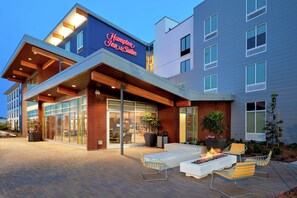 A modern hotel exterior with a prominent sign, outdoor seating area, and large windows. - Hampton Inn & Suites San Diego Airport Liberty Station (San Diego)