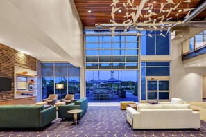 A spacious lobby with a large seating area, a wooden ceiling, and large windows offering a view of the outdoor patio area. - Hampton Inn & Suites San Diego Airport Liberty Station (San Diego)