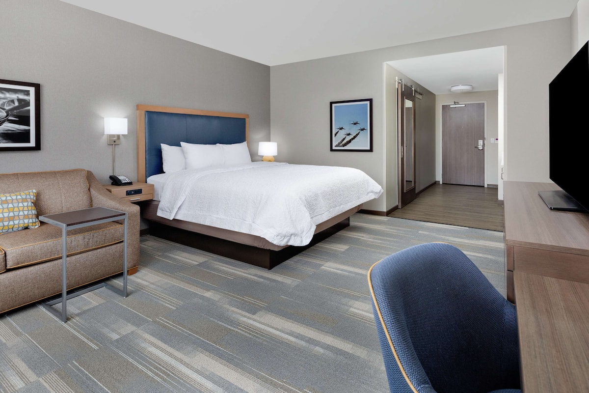 A hotel room with a bed, a desk, a chair, a sofa, a bedside table, and a TV.