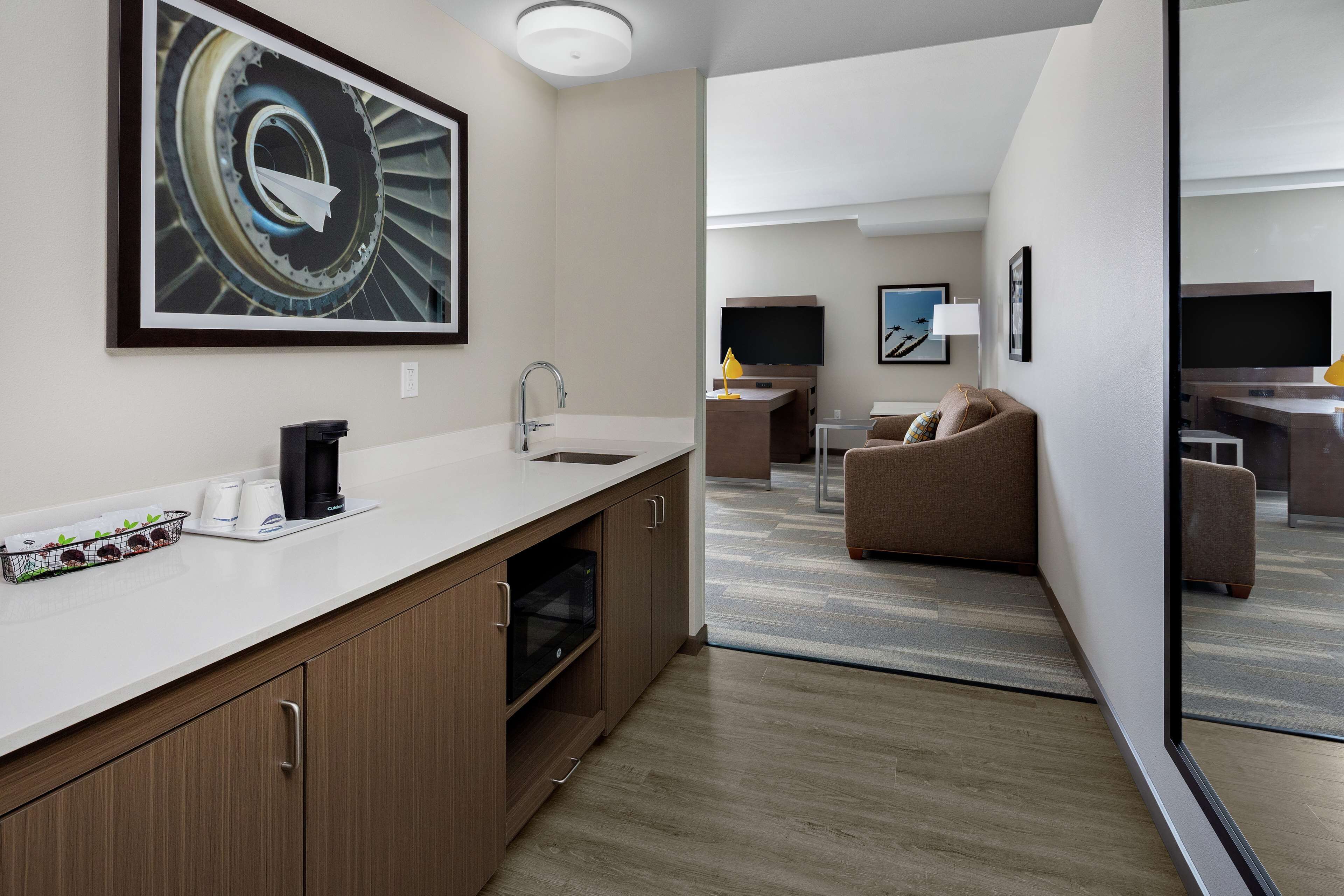 A modern hotel room with a kitchenette, a large window, and a seating area with a sofa and armchairs.