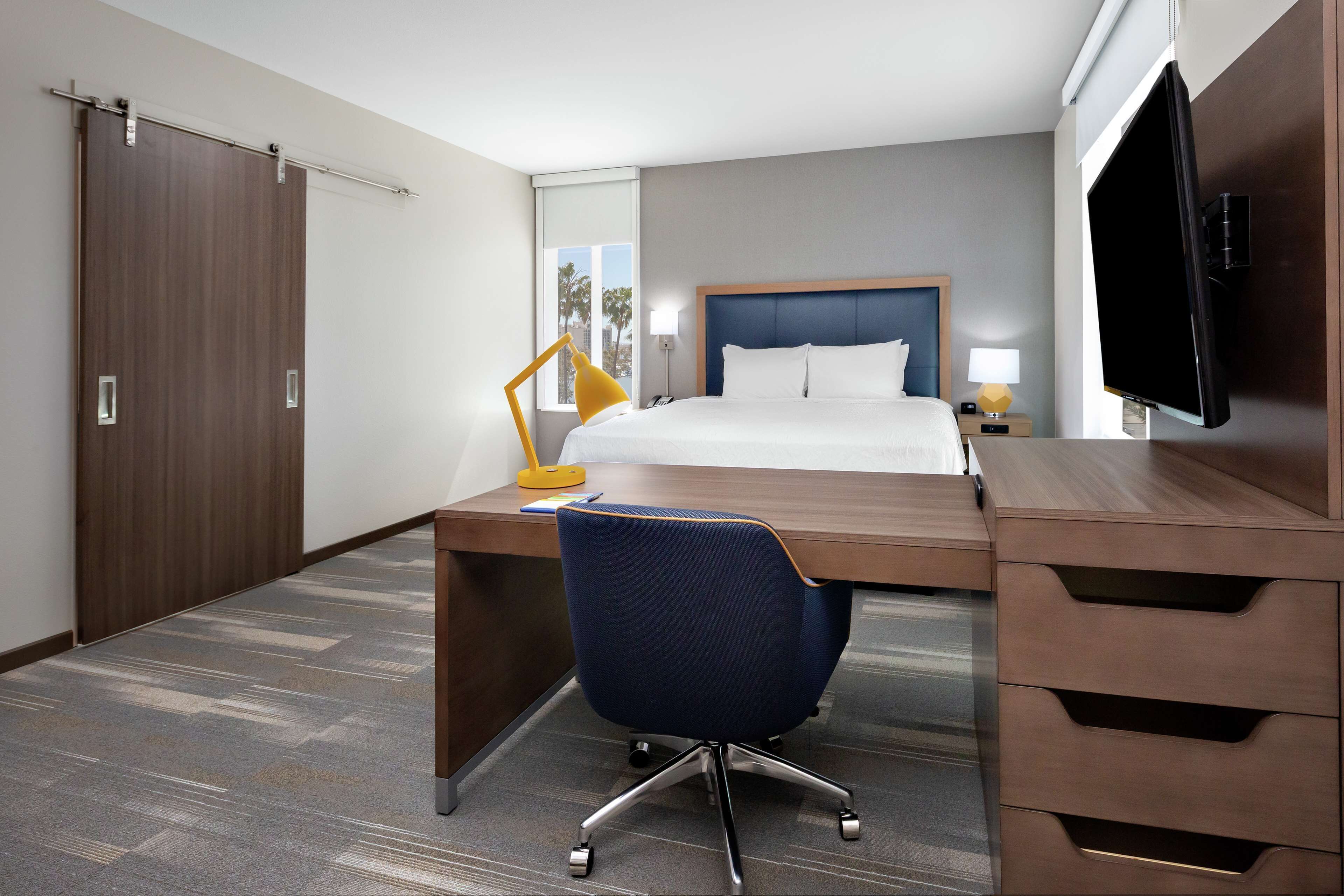 A hotel room with a bed, desk, chair, TV, and wardrobe.