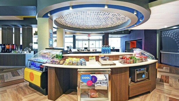 A modern self-service kiosk with a refrigerated section, a coffee machine, and a variety of packaged snacks. - Tru by Hilton Grand Rapids Airport (Grand Rapids)