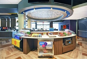 A modern self-service kiosk with a refrigerated section, a coffee machine, and a variety of packaged snacks. - Tru by Hilton Grand Rapids Airport (Grand Rapids)