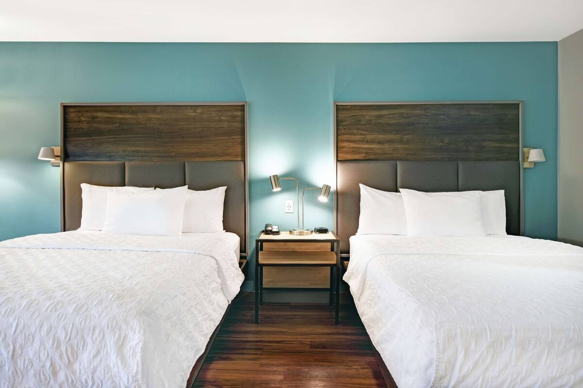 A hotel room with two beds, a wooden nightstand, and a lamp between them.