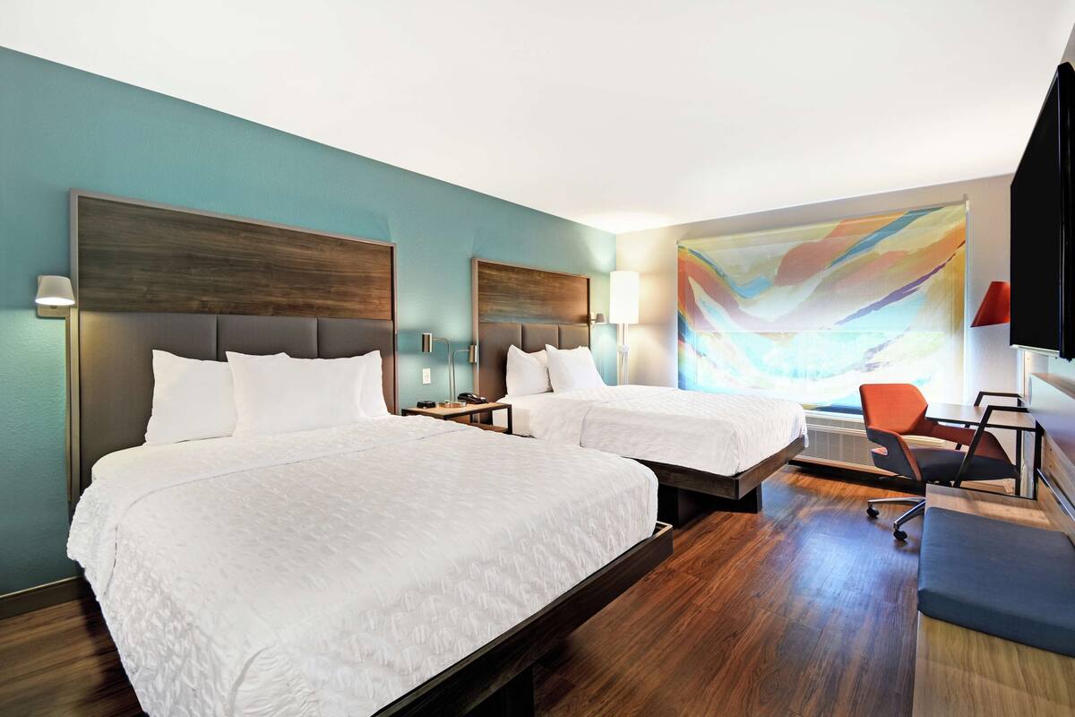 A hotel room with two beds, a desk, a chair, and a large abstract painting on the wall.