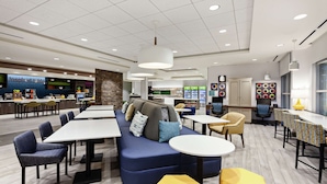 Een moderne eethoek met een blauwe bank, een geel poef en meerdere tafels en stoelen.