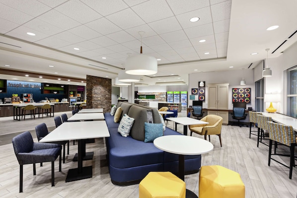 A modern dining area with a blue sofa, yellow ottoman, and multiple tables and chairs.