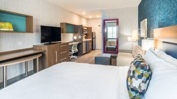 Une chambre d’hôtel avec un lit, un bureau, une télévision, une chaise, une petite table, un miroir et une fenêtre.