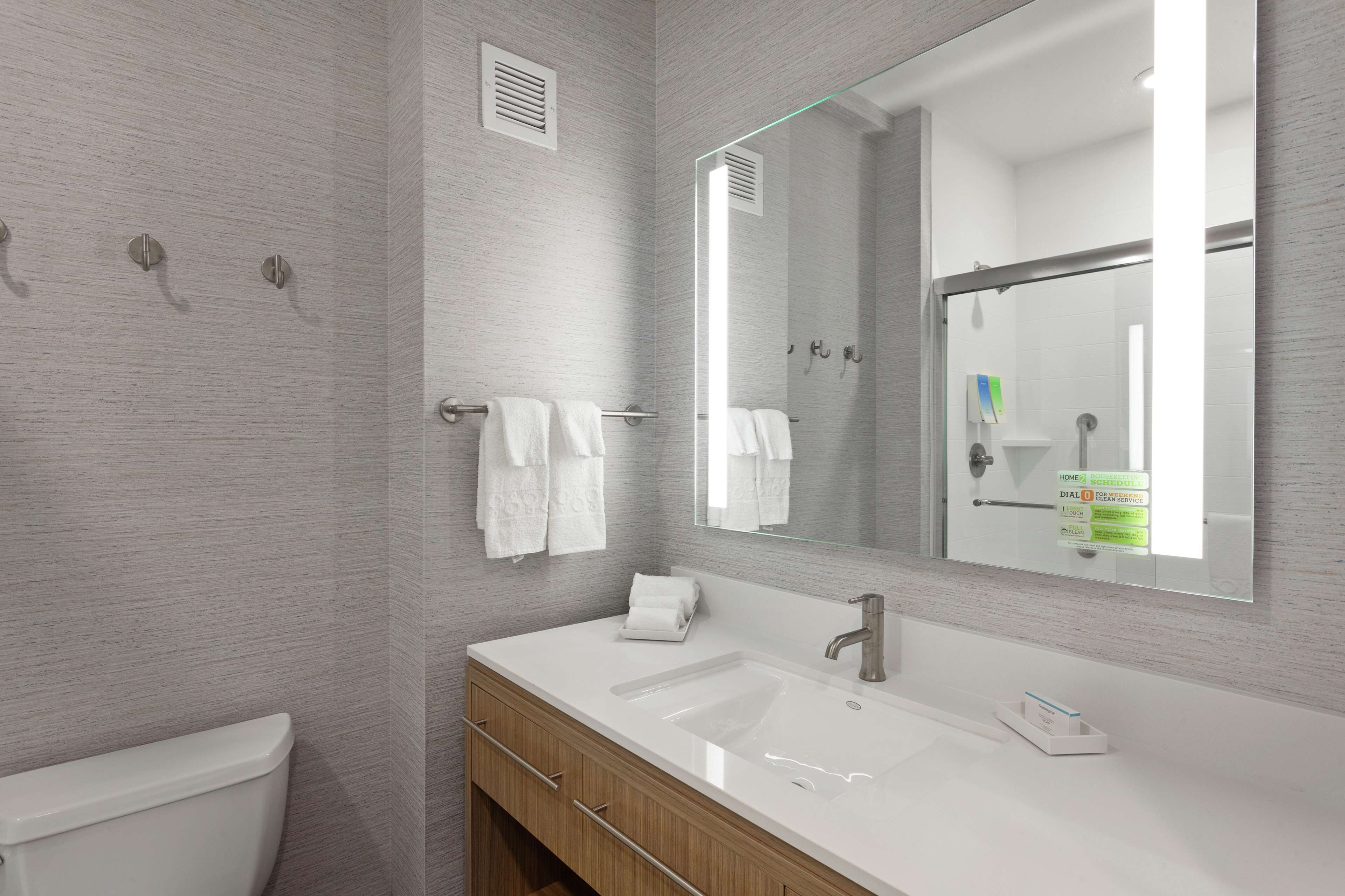 A modern bathroom with a white sink, wooden vanity, and a large mirror.