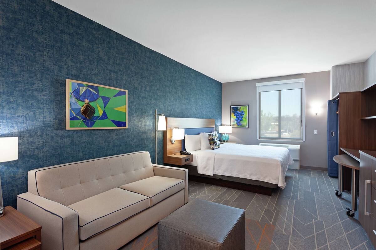 A hotel room with a bed, a sofa, a desk, and a nightstand.
