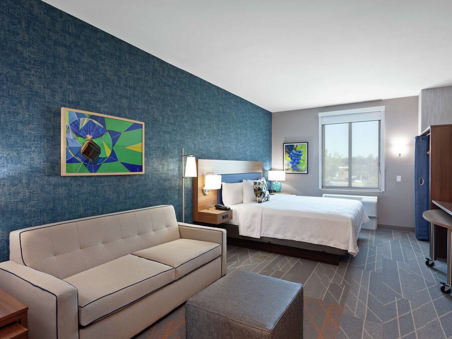 A hotel room with a bed, a sofa, a desk, and a nightstand.