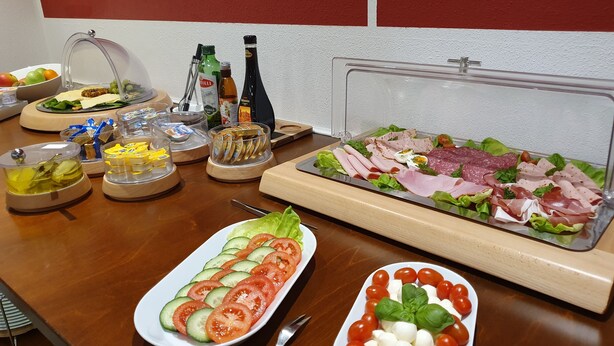A buffet table with various food items including a salad, sliced cucumbers, tomatoes, mozzarella, and a variety of meats.