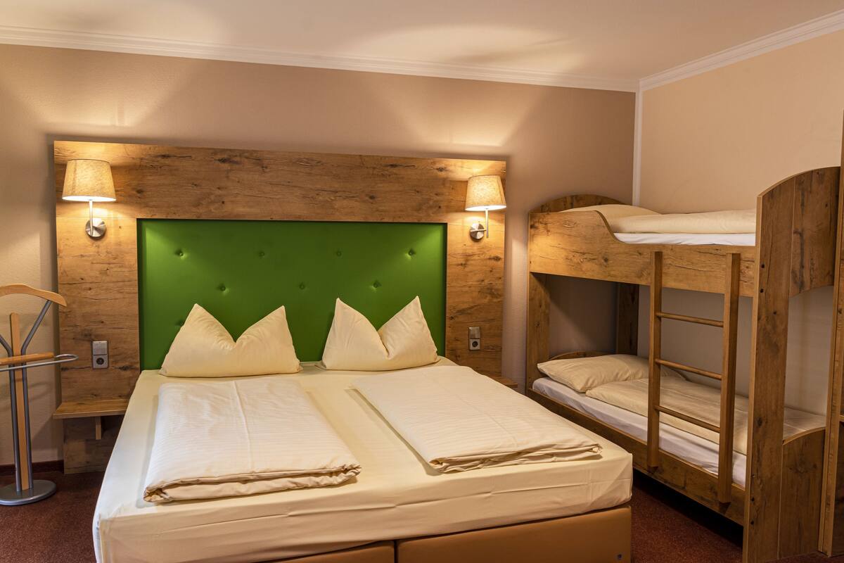 Ein Hotelzimmer mit einem großen Bett, einem Etagenbett, einem Holzkopfteil und zwei Wandleuchten.