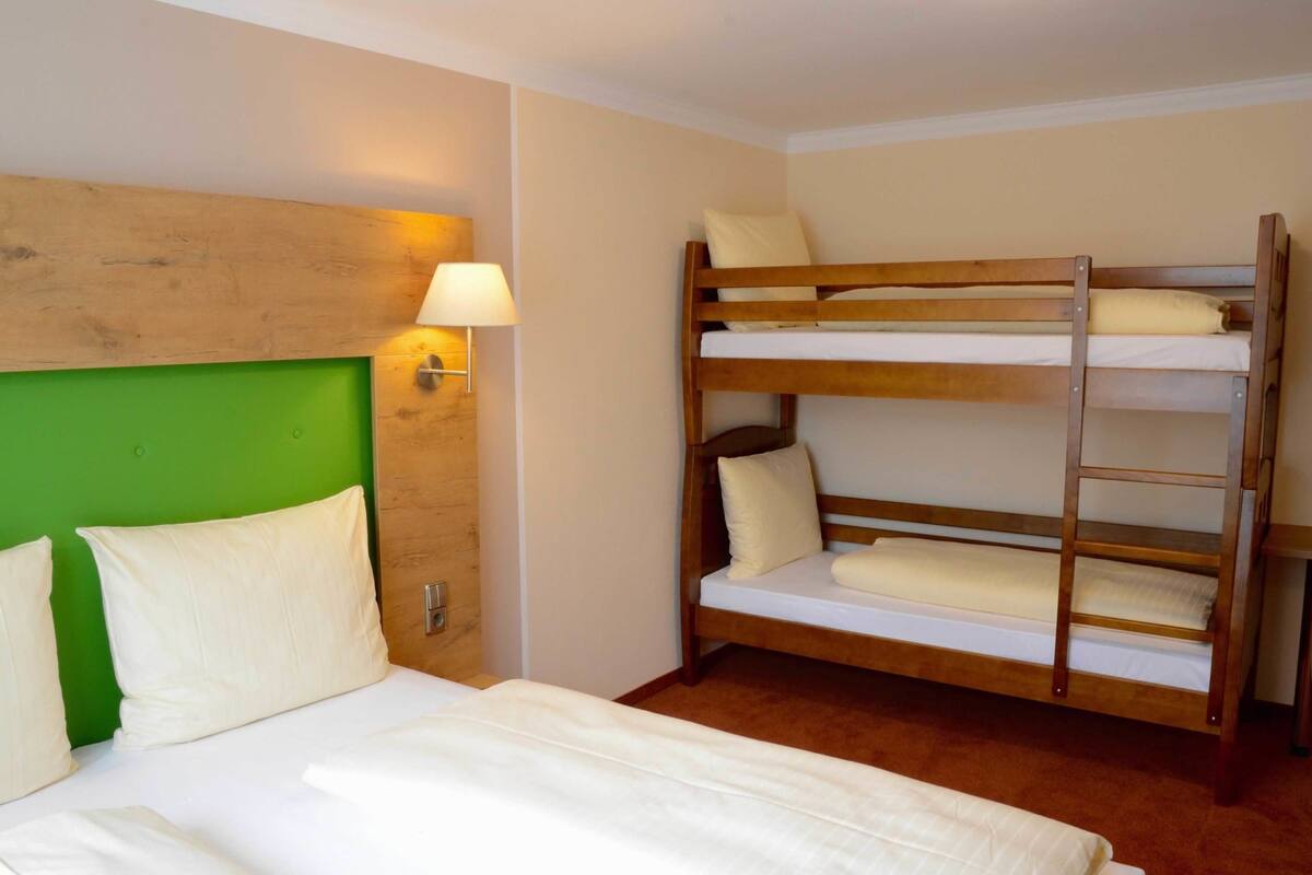 Ein Hotelzimmer mit Etagenbett, einem grünen Kopfteil, einer Nachttischlampe und Holzboden.