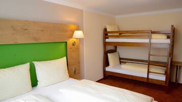 Quarto de hotel com cama de beliche, cabeceira verde, luminária de cabeceira e piso de madeira.