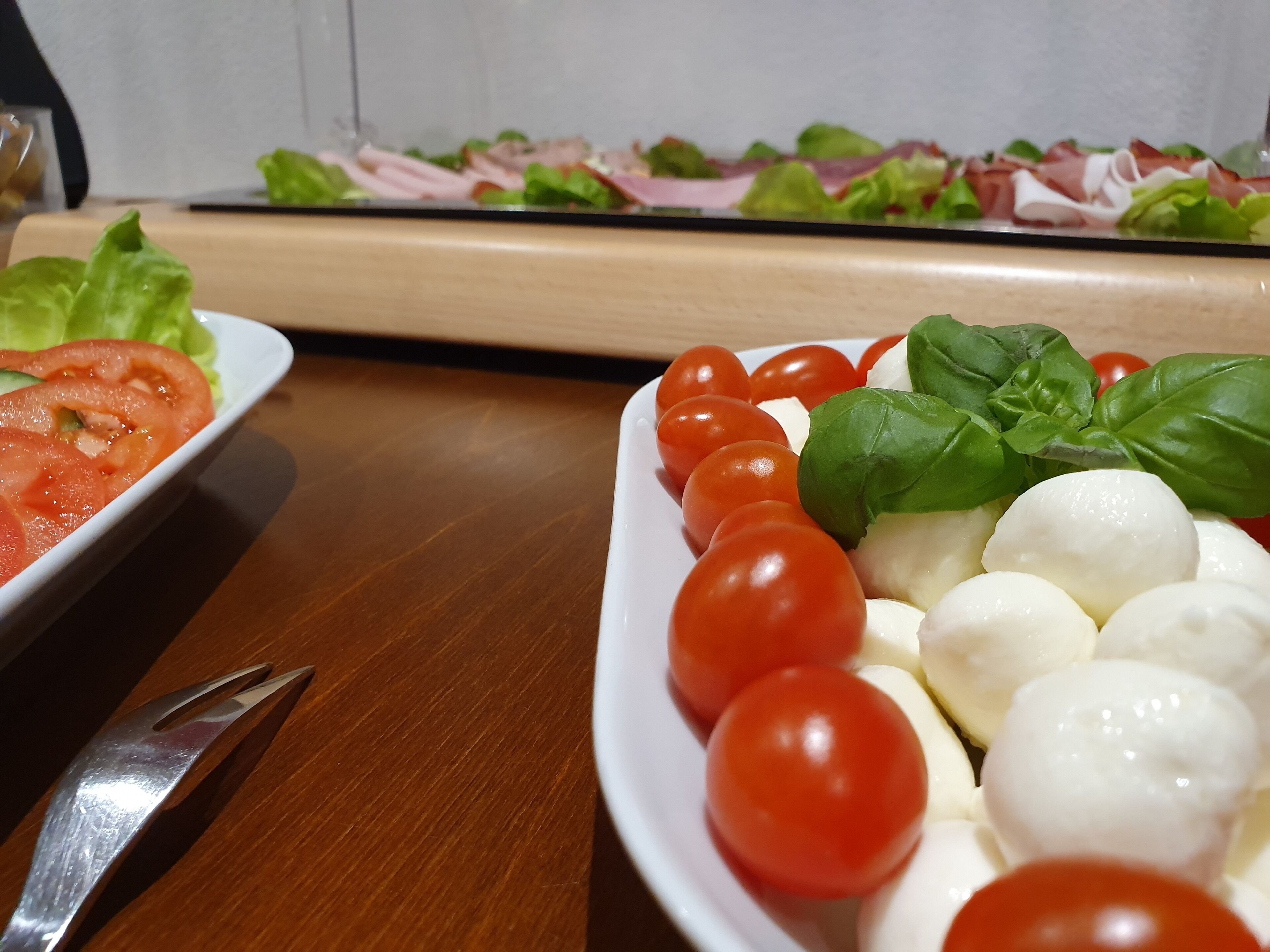 Una mesa de madera con dos platos de comida, uno con tomates y albahaca y el otro con mozzarella y tomates.