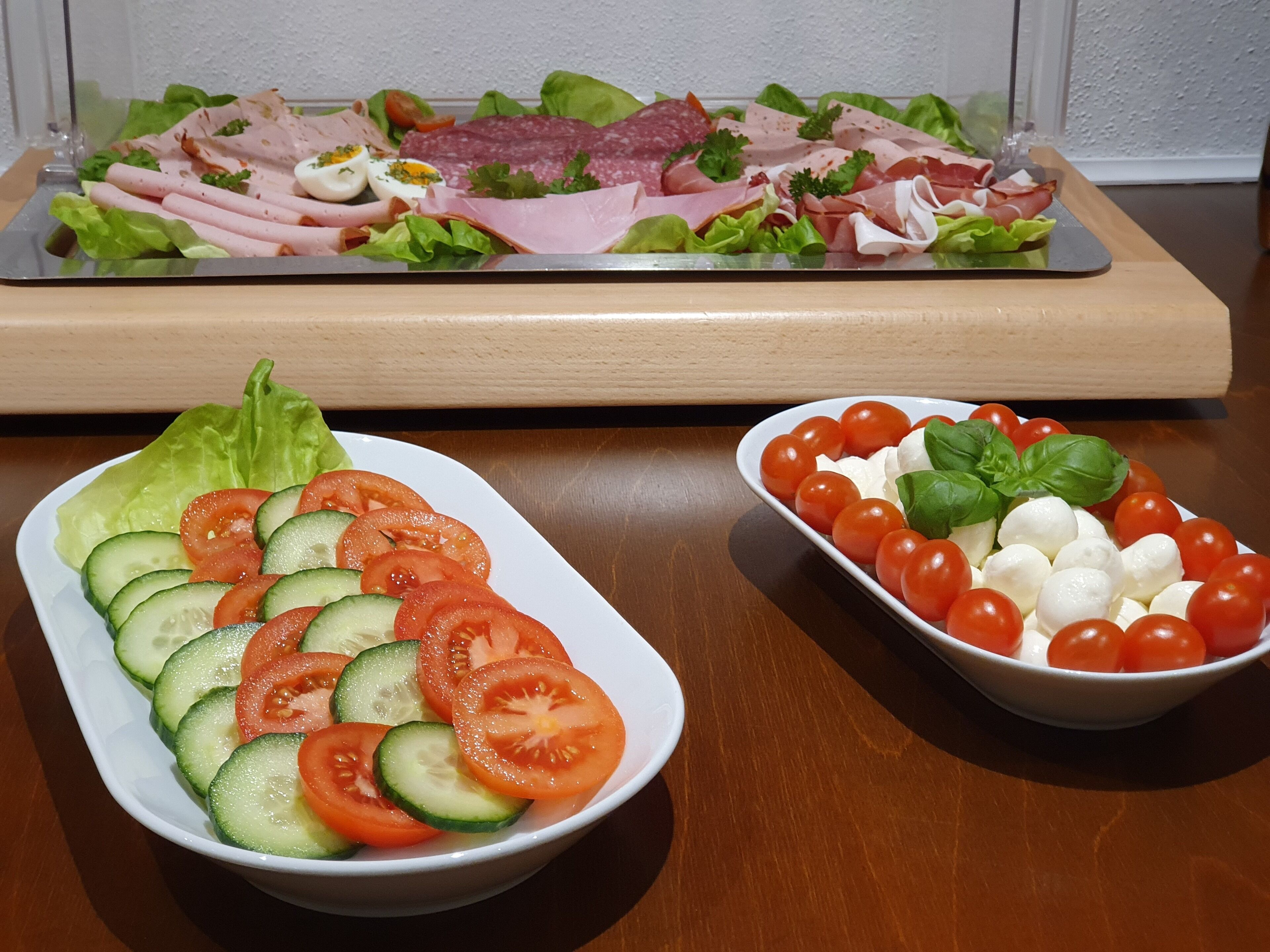 Una mesa con dos platos: uno con pepinos y tomates en rodajas, y otro con tomates cherry y bolas de mozzarella.