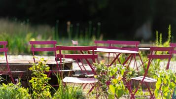 Espace extérieur aménagé avec des chaises et des tables en métal, entouré de verdure.