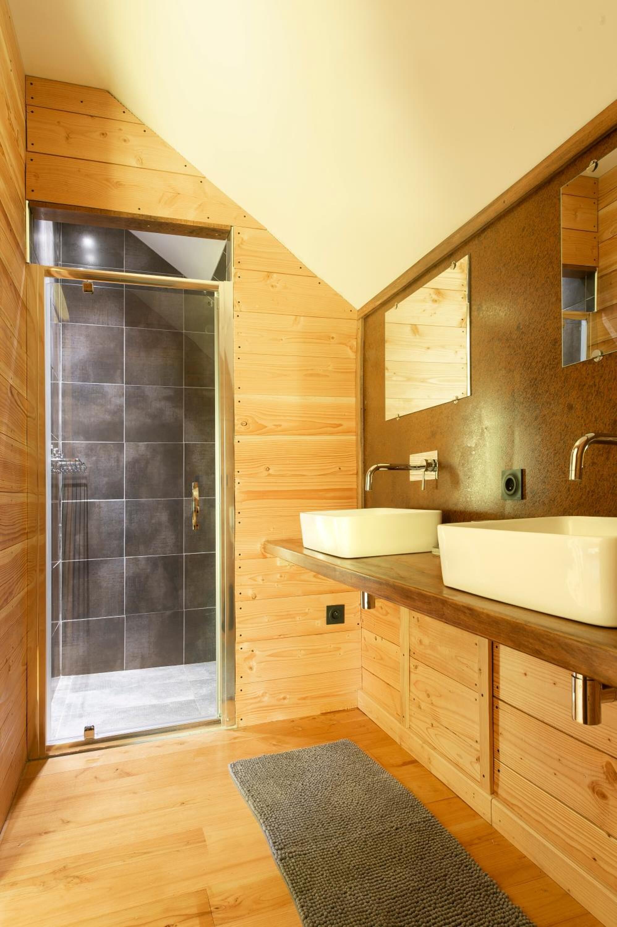 Un baño moderno con paredes de madera, cabina de ducha de vidrio y un espejo grande sobre el lavabo.