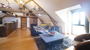 A loft-style living space with exposed wooden beams, a loft bed, a dining area, and a kitchen with a brick wall. - Ecolodges de Loire & Spa (Gennes-Val-de-Loire)