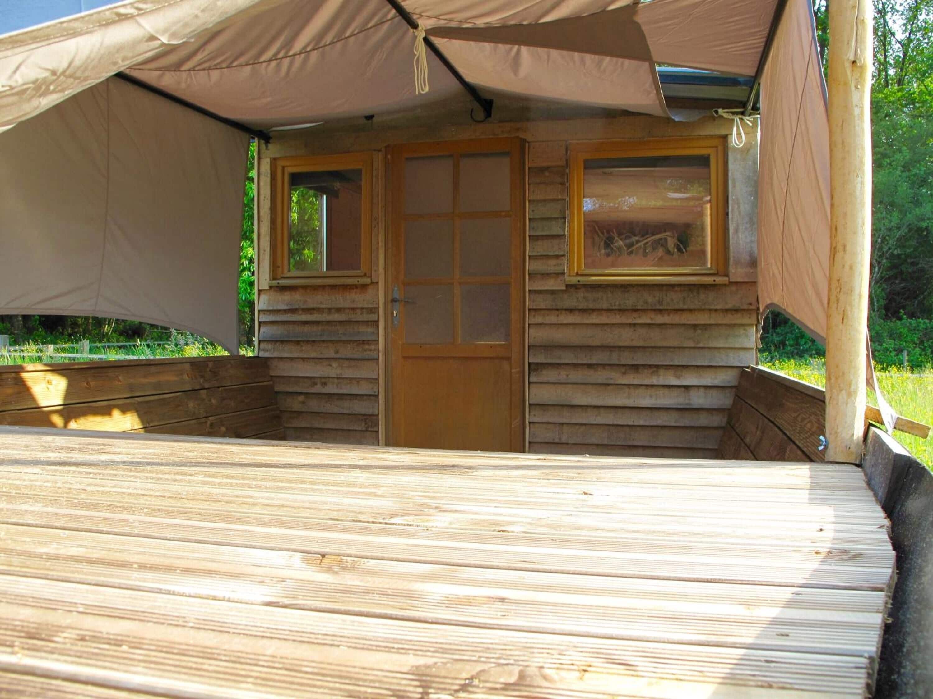 Una terraza de madera con una carpa encima, una puerta de madera y dos ventanas.
