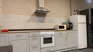 A kitchen with white cabinets, a microwave, a stove, and a refrigerator. - Albergue La Estación - Hostel (Llanes)