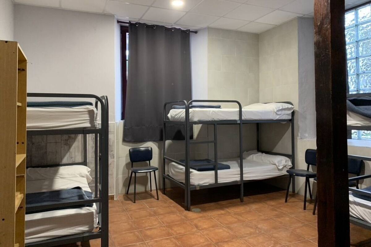 A dormitory room with bunk beds, a chair, and a window.