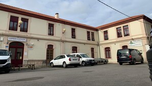 A building with a sign reading "Albergue La Estacion" indicating a hostel. There are parked cars and a bench in front. - Albergue La Estación - Hostel (Llanes)