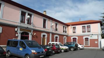 A parking lot with several cars parked in front of a building with a red roof and pink walls.