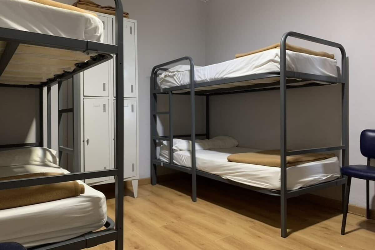A dormitory room with bunk beds, a desk, and a chair.
