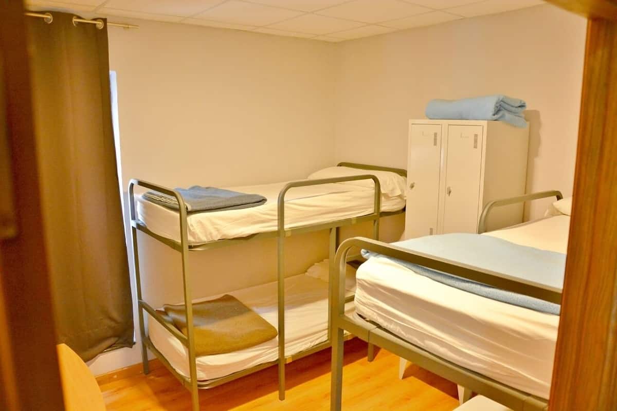 A dormitory room with bunk beds, a wardrobe, and a curtain.