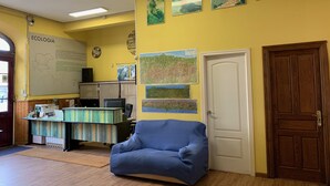 A room with a wooden floor, a blue chair, a desk with a computer, and a white door. - Albergue La Estación - Hostel (Llanes)