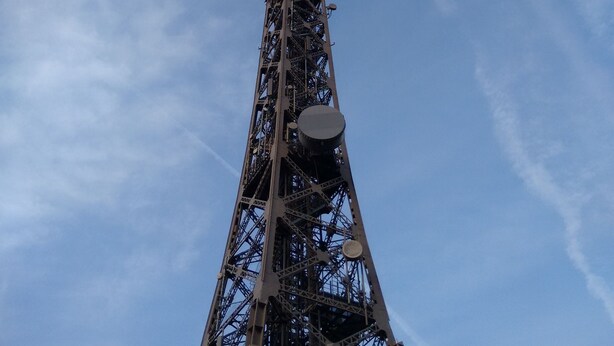A tall, metal tower structure with a cylindrical top, likely a communication or observation tower, set against a clear blue sky with some clouds. - Serenity Guesthouse (Beaune)
