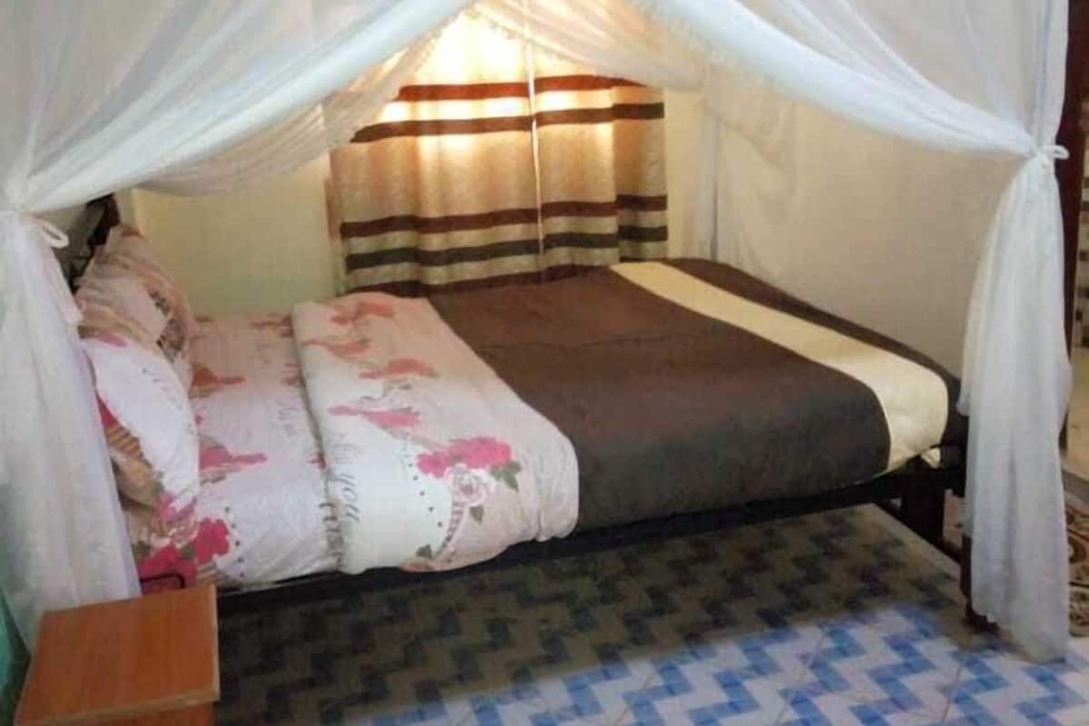 A single bed with a canopy, a bedside table, and a patterned floor.