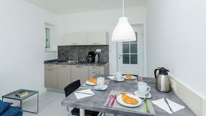 A compact kitchen with a dining area, a coffee maker, a kettle, and breakfast items on the table.