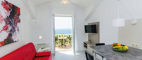 Una habitación moderna con un sofá rojo, una mesa de comedor con fruta, un televisor y un balcón con vistas.