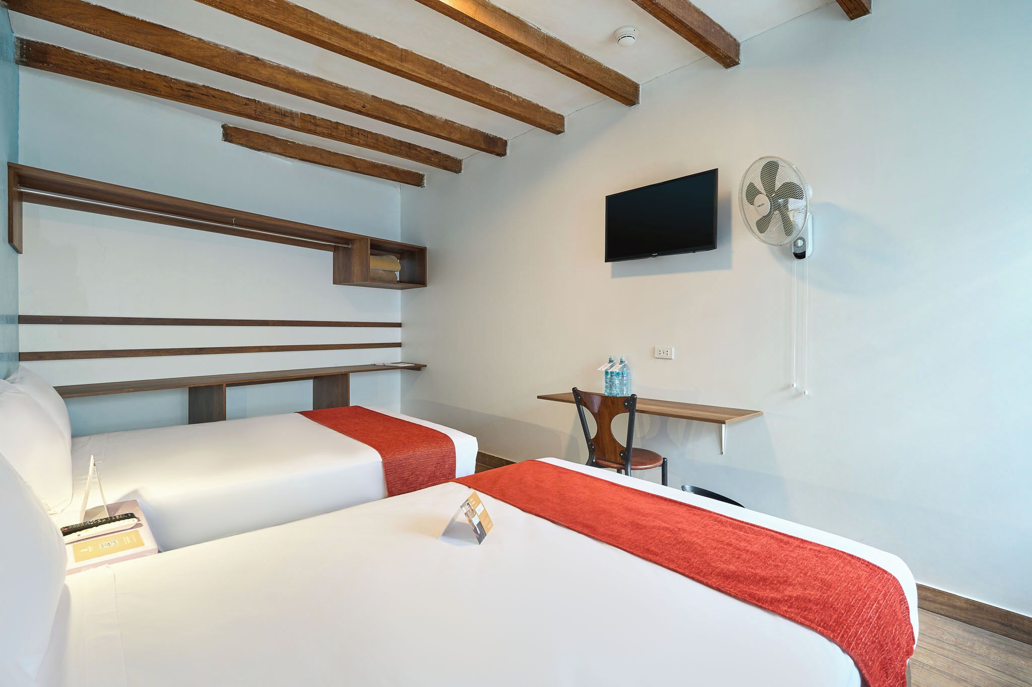 Una habitación de hotel con dos camas, televisión, ventilador y una mesita.