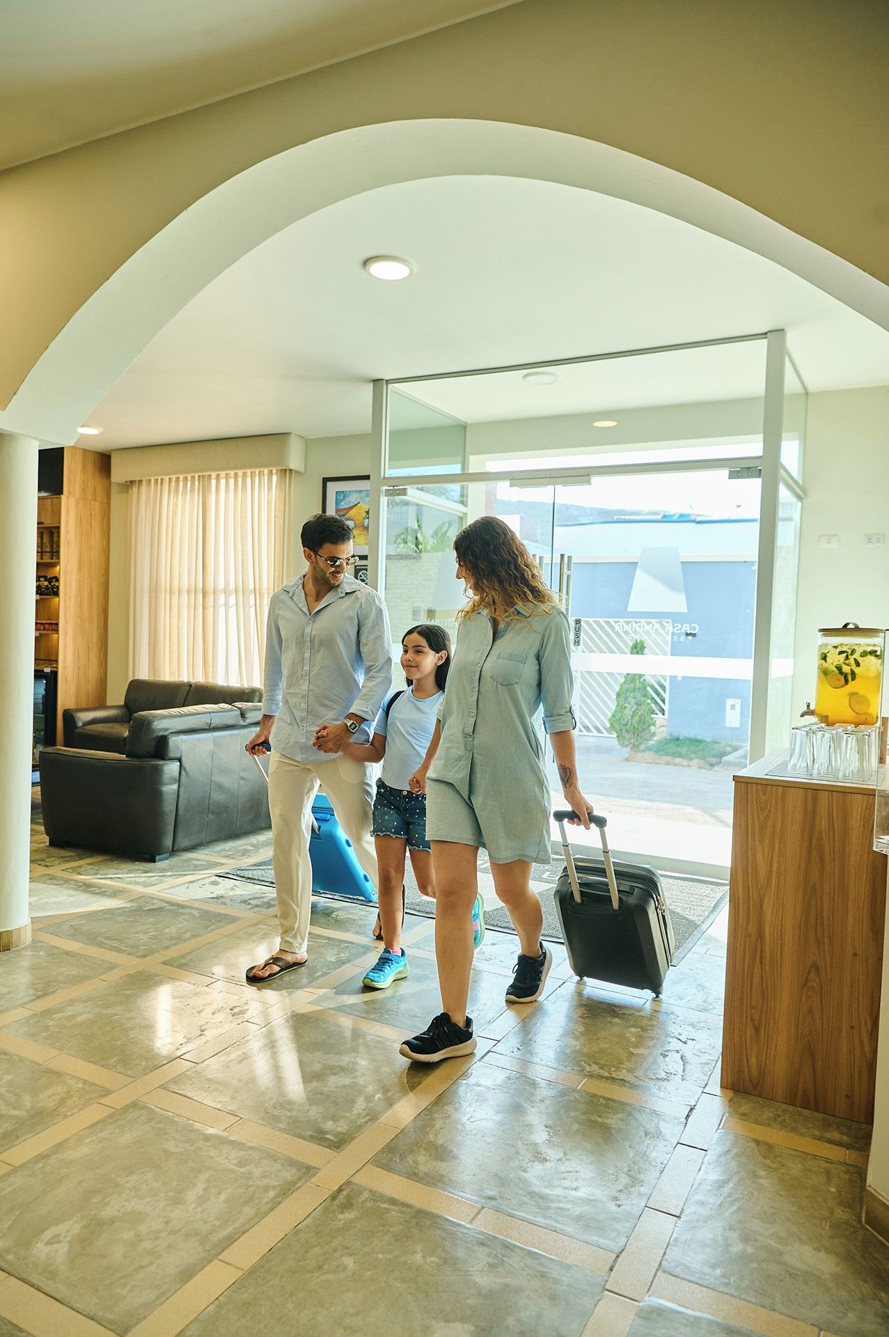 Una familia en un moderno vestíbulo de hotel con un separador de vidrio, una zona de estar y vistas al exterior.