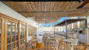 Un área de patio al aire libre con mesas y sillas, techo de madera y vistas de los edificios circundantes.