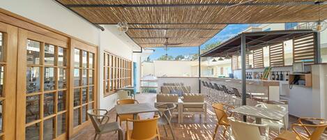 Un área de patio al aire libre con mesas y sillas, techo de madera y vistas de los edificios circundantes.