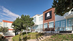 A hotel with a prominent sign, a staircase, and a landscaped area with trees. - Casa Andina Standard Ica   (Ica)