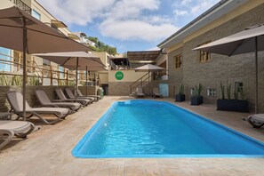 A swimming pool with lounge chairs and umbrellas, surrounded by stone walls and a building with a sign. - Casa Andina Standard Ica   (Ica)