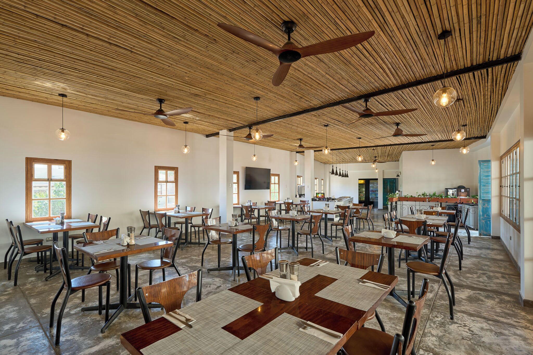 A spacious dining area with multiple tables and chairs, ceiling fans, and hanging lights.