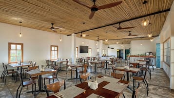 A spacious dining area with multiple tables and chairs, ceiling fans, and hanging lights.